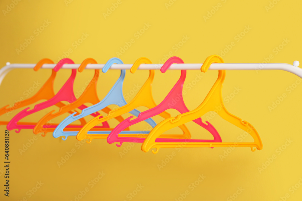 Rack with plastic clothes hangers on yellow background