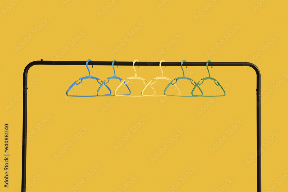 Rack with plastic clothes hangers on yellow background