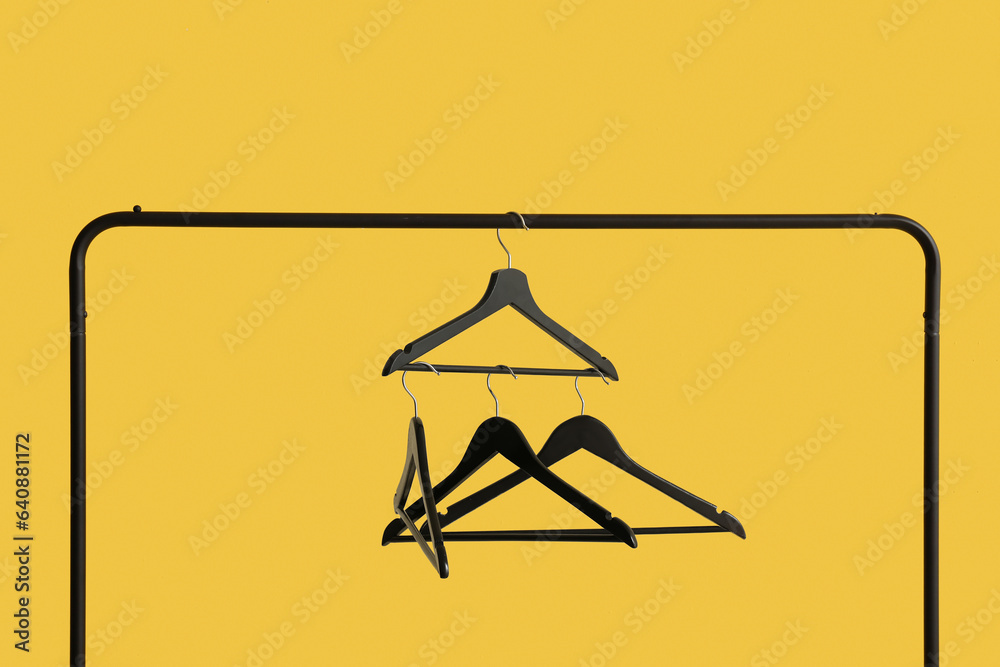 Rack with wooden clothes hangers on yellow background