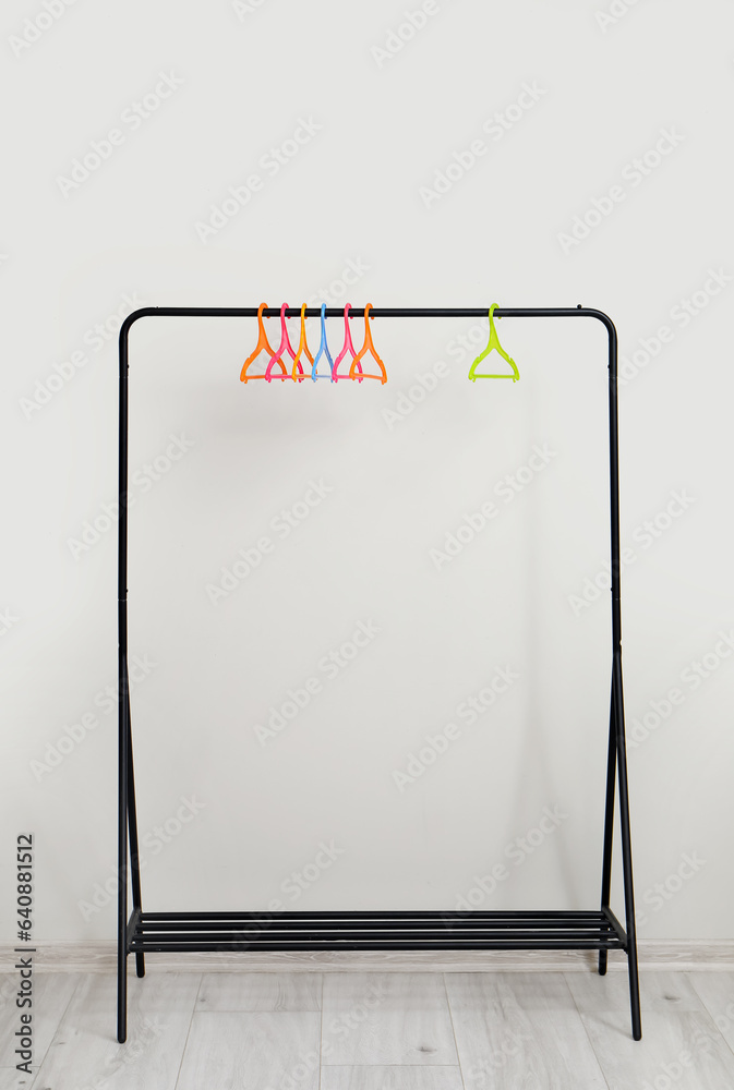 Rack with plastic clothes hangers near grey wall