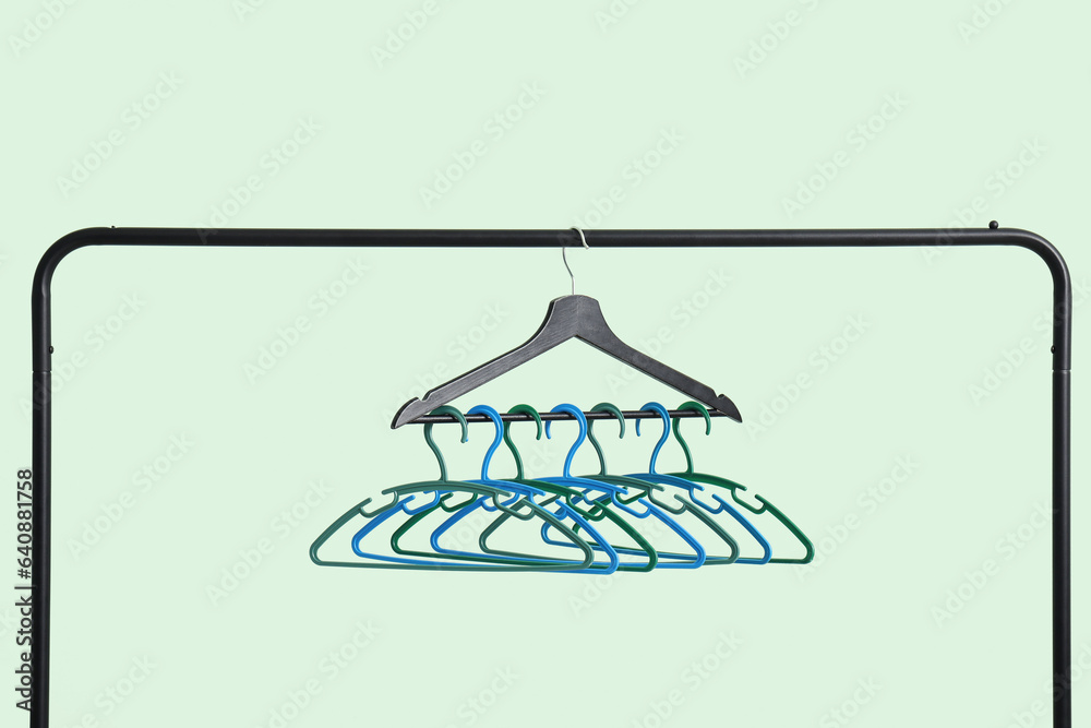 Rack with plastic clothes hangers on green background