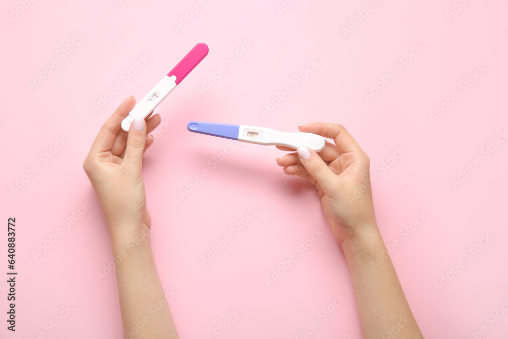 Female hands with pregnancy tests on pink background