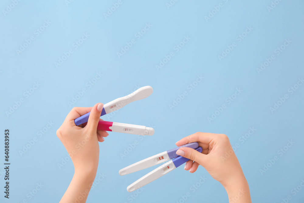 Female hands with different pregnancy tests on color background