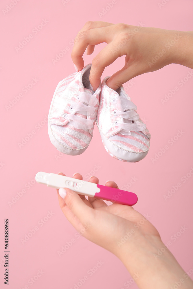 Female hands with pregnancy test and baby booties on pink background, closeup