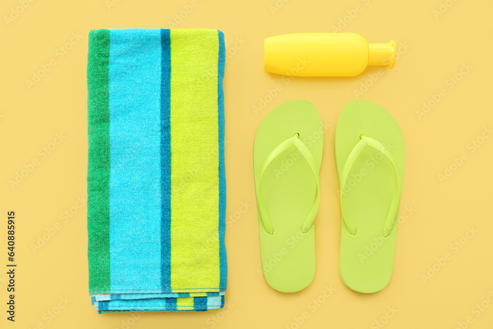 Pair of green flip flops with blanket and sunscreen cream on yellow background