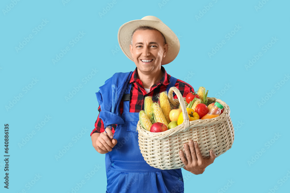 Mature male farmer with wicker basket full of different ripe vegetables on blue background