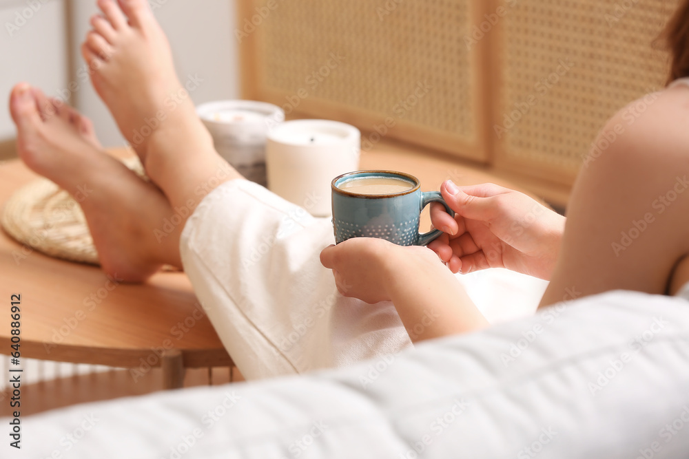 Woman with cup of tasty coffee resting on sofa at home