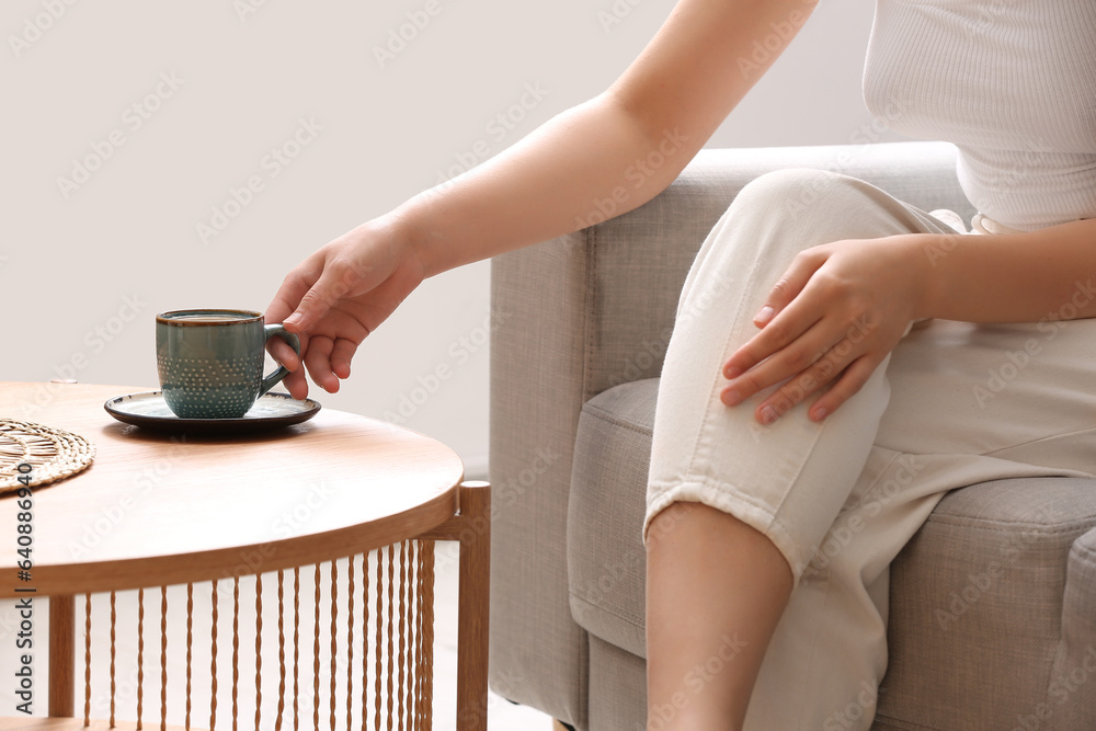 Woman taking cup of tasty coffee from table at home