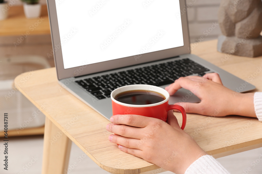 Woman with cup of coffee working on laptop at home