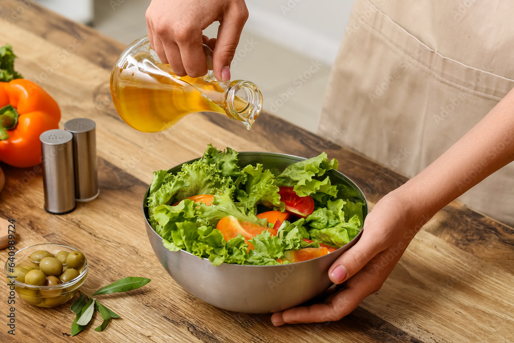 Woman adding olive oil into bowl with tasty salad at table in kitchen