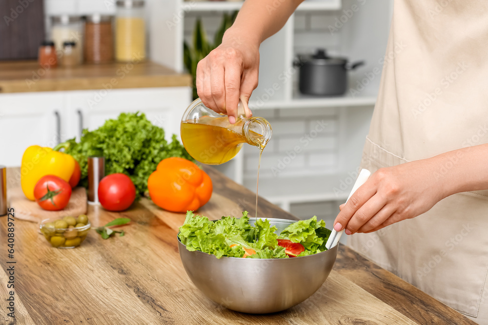 Woman adding olive oil into bowl with tasty salad at table in kitchen