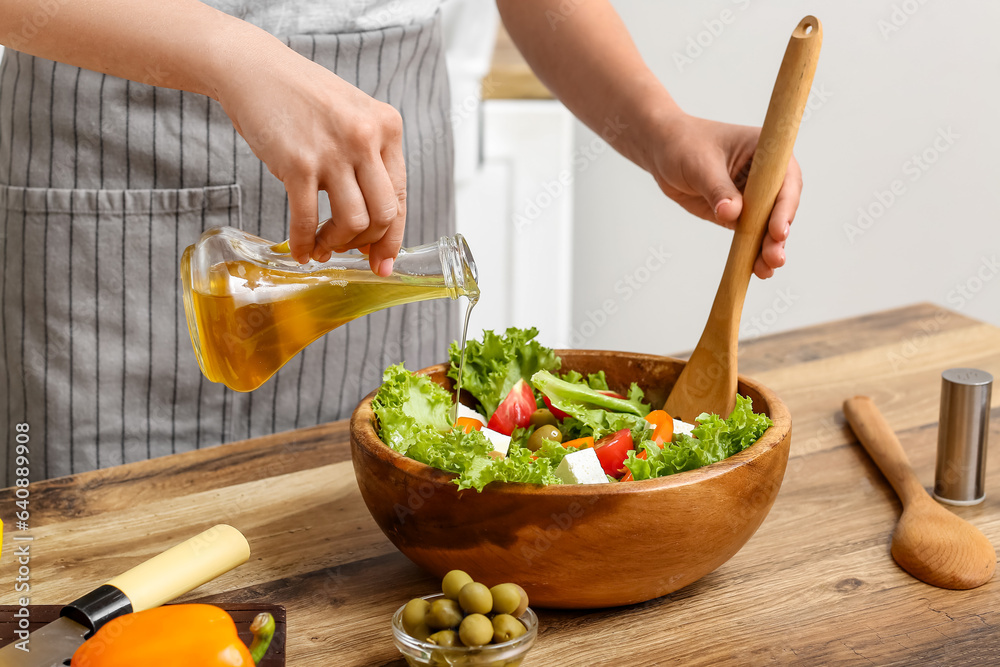 Woman adding olive oil into bowl with tasty salad at table in kitchen