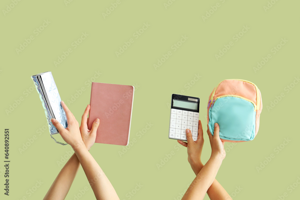 Female hands with backpack and different stationery on green background