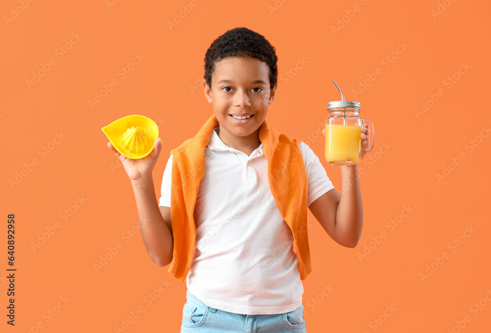 Little African-American boy with mason jar of fresh citrus juice and squeezer on orange background