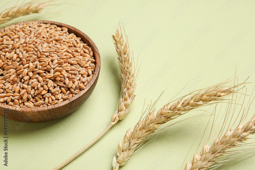 Wooden bowl with grains and wheat ears on light green background