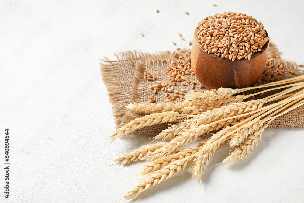 Wooden bowl with grains, wheat ears and fabric on white background