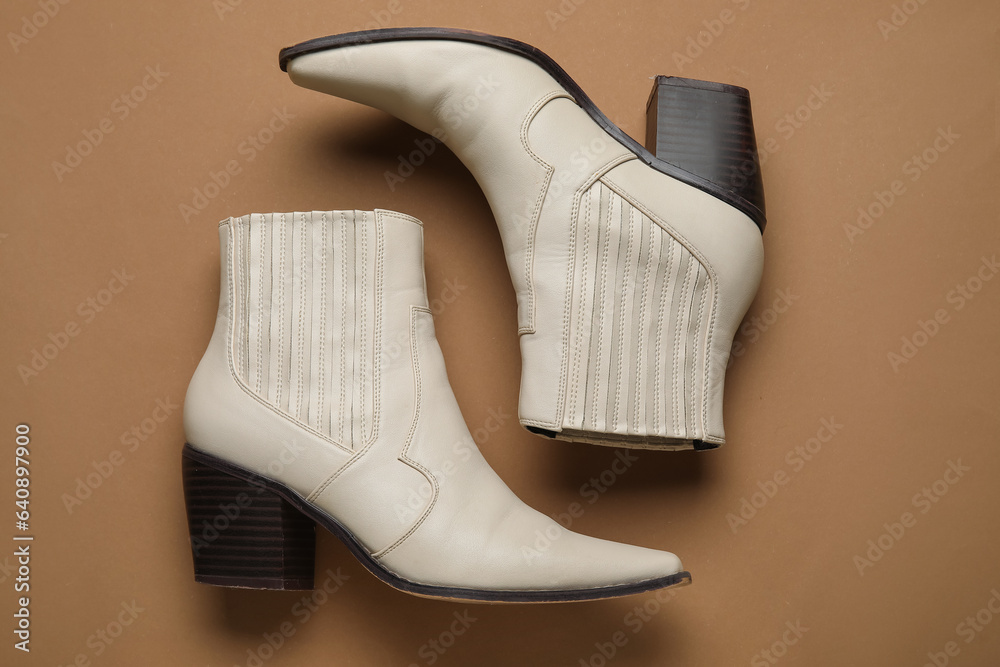 Stylish white leather boots on brown background