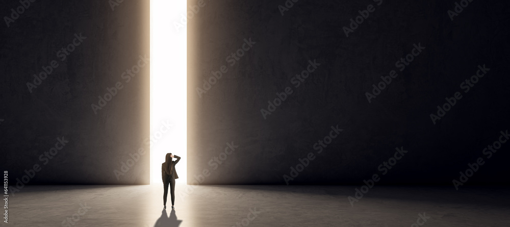 Back view of thoughtful young businesswoman looking at bright line opening on black concrete wall ba