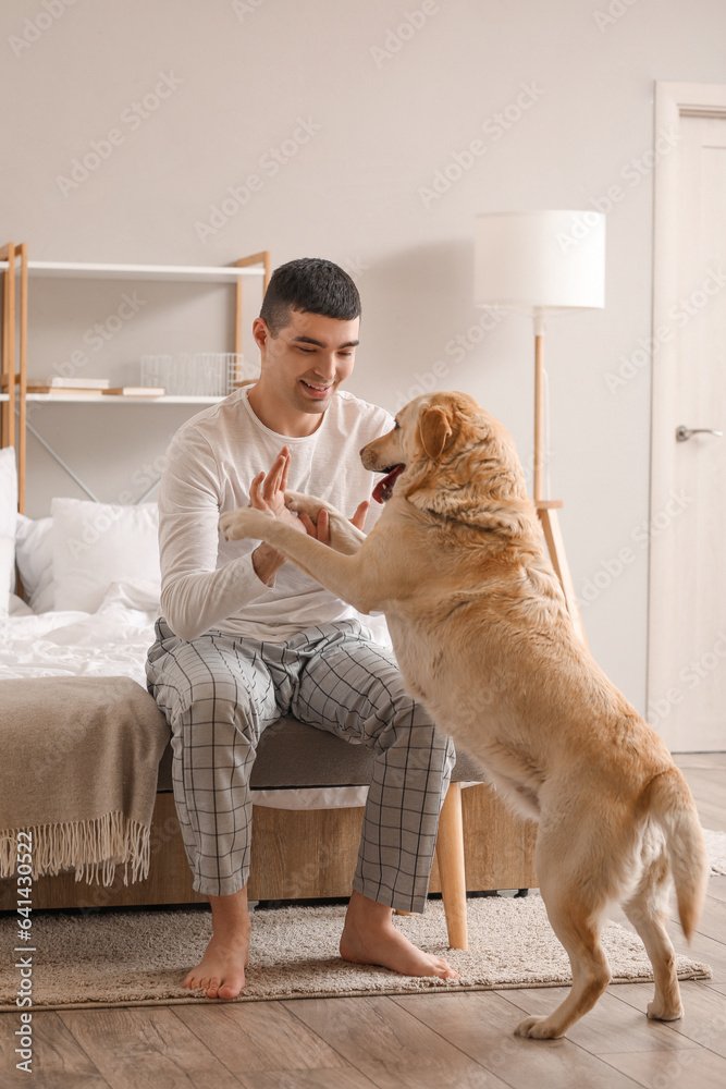 Young man with cute Labrador dog sitting in bedroom