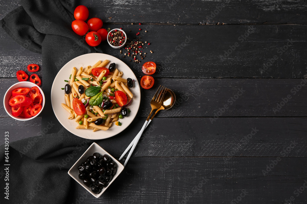 Plate with tasty pasta salad and ingredients on dark wooden background