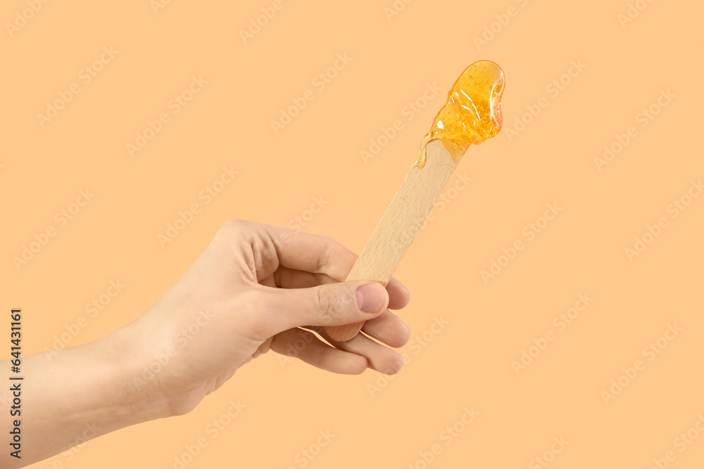 Female hand holding spatula with sugaring paste on beige background