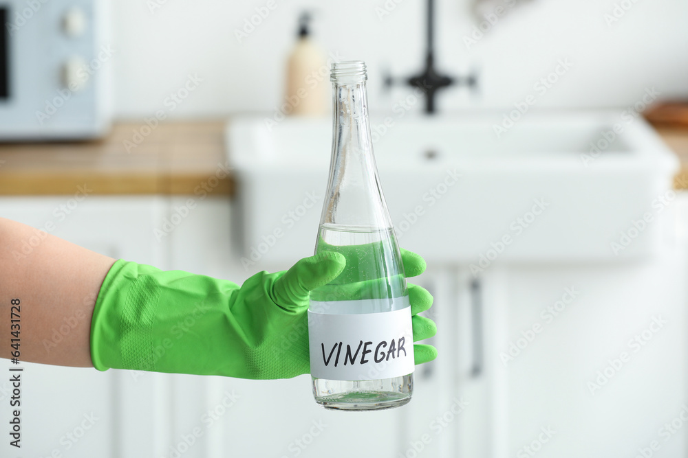 Female hand in rubber glove with bottle of vinegar in kitchen