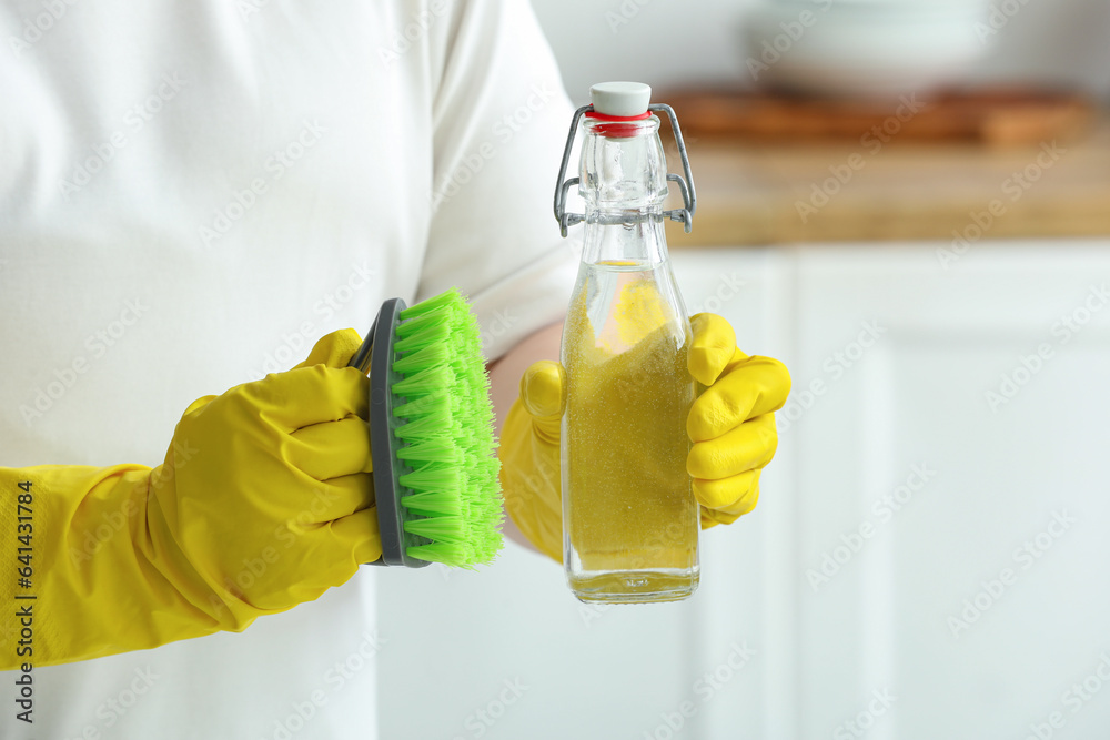 Woman with bottle of vinegar and brush in kitchen, closeup