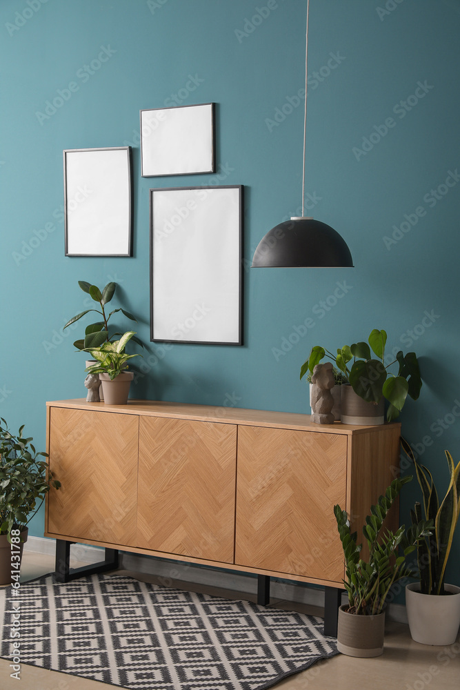 Table with green houseplants and blank frames on blue wall in room