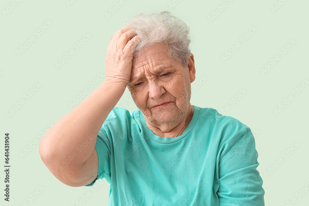 Upset senior woman on green background, closeup