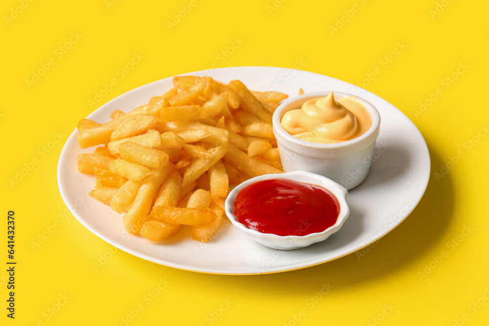 Plate with tasty french fries and sauces on yellow background