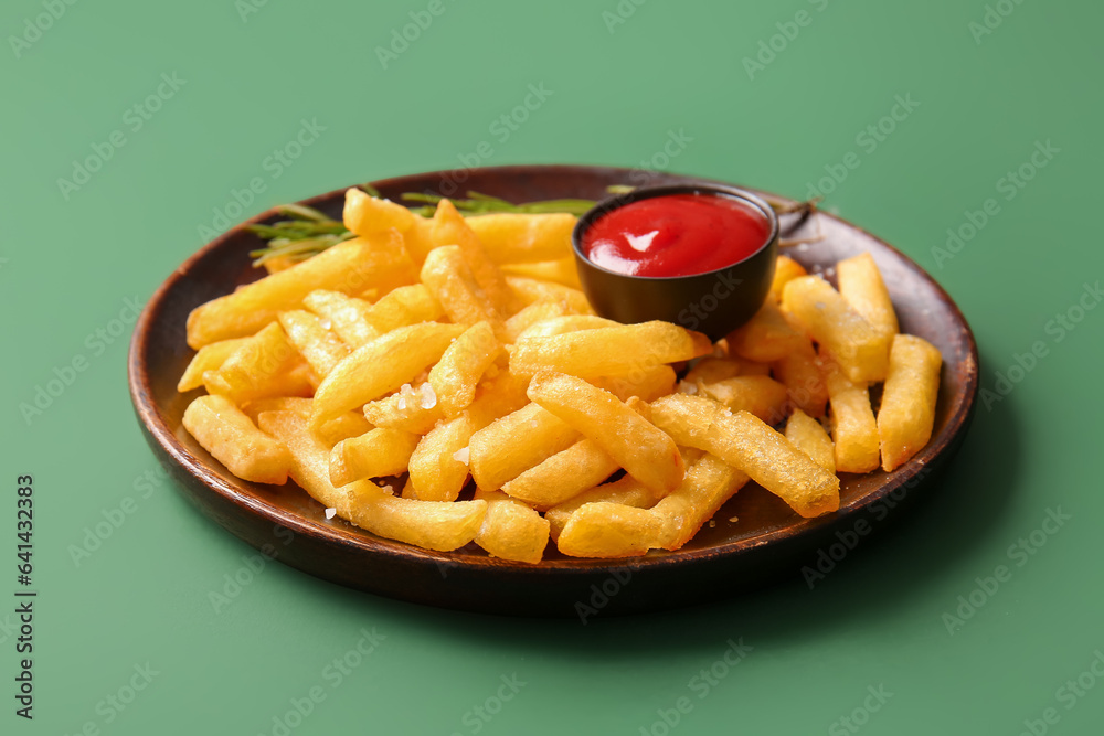 Plate with tasty french fries and ketchup on green background