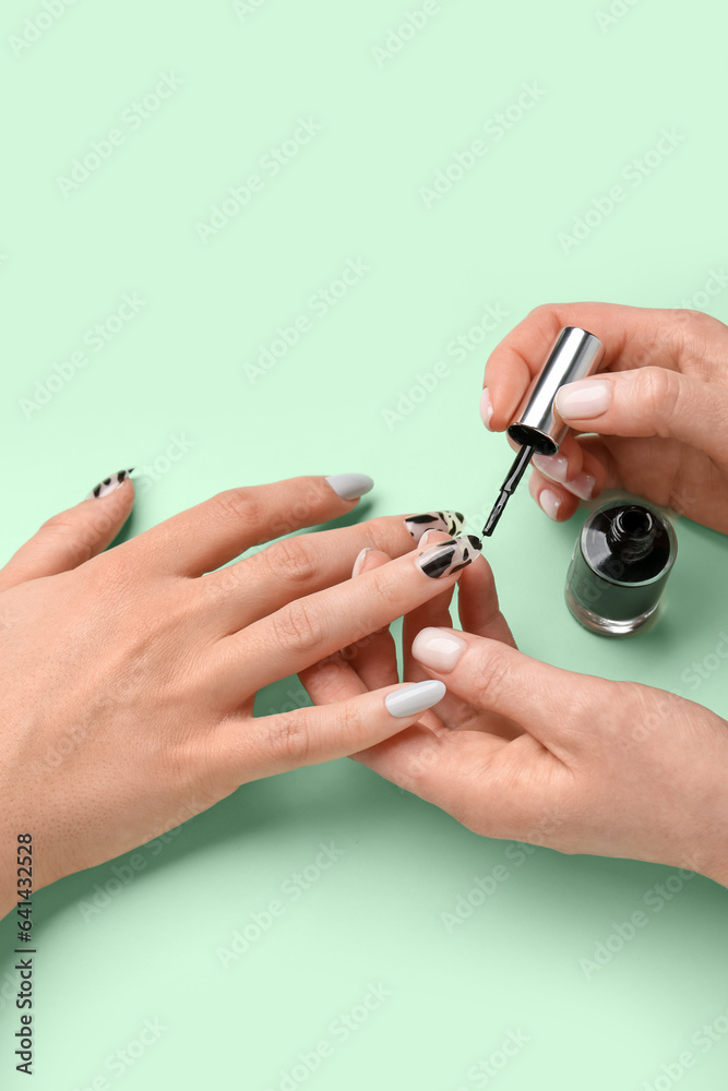 Manicure master applying polish onto press-on nail on green background, closeup