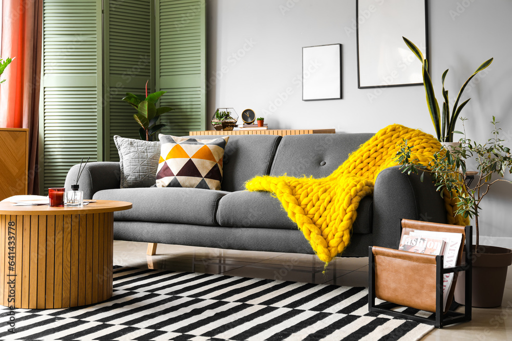 Interior of stylish living room with cozy grey sofa and reed diffuser on coffee table