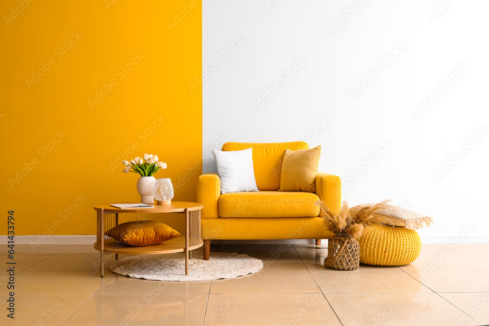 Cozy armchair and coffee table with tulip flowers in vase near colorful wall