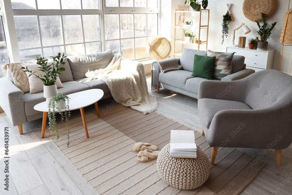 Interior of bright living room with cozy sofas and armchair near big window