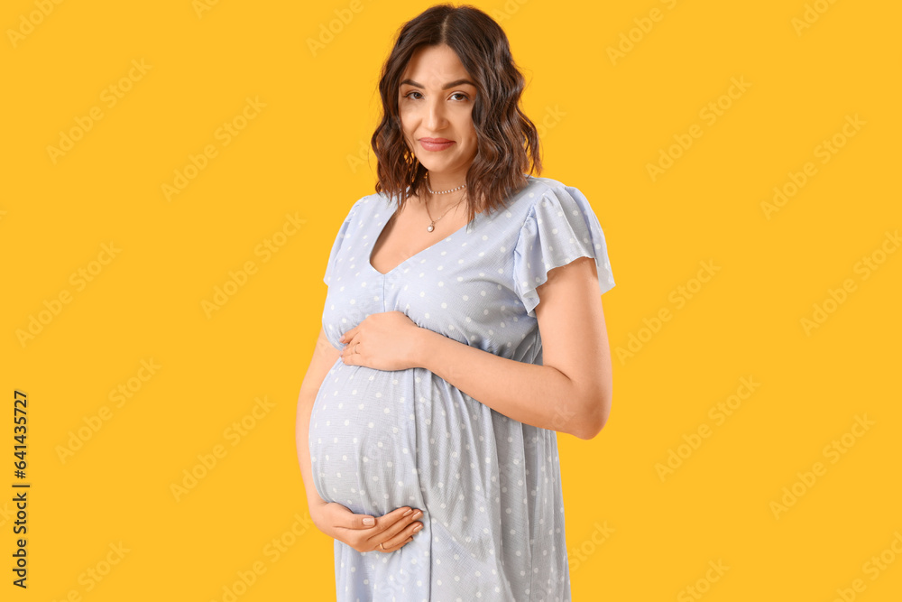 Young pregnant woman on yellow background