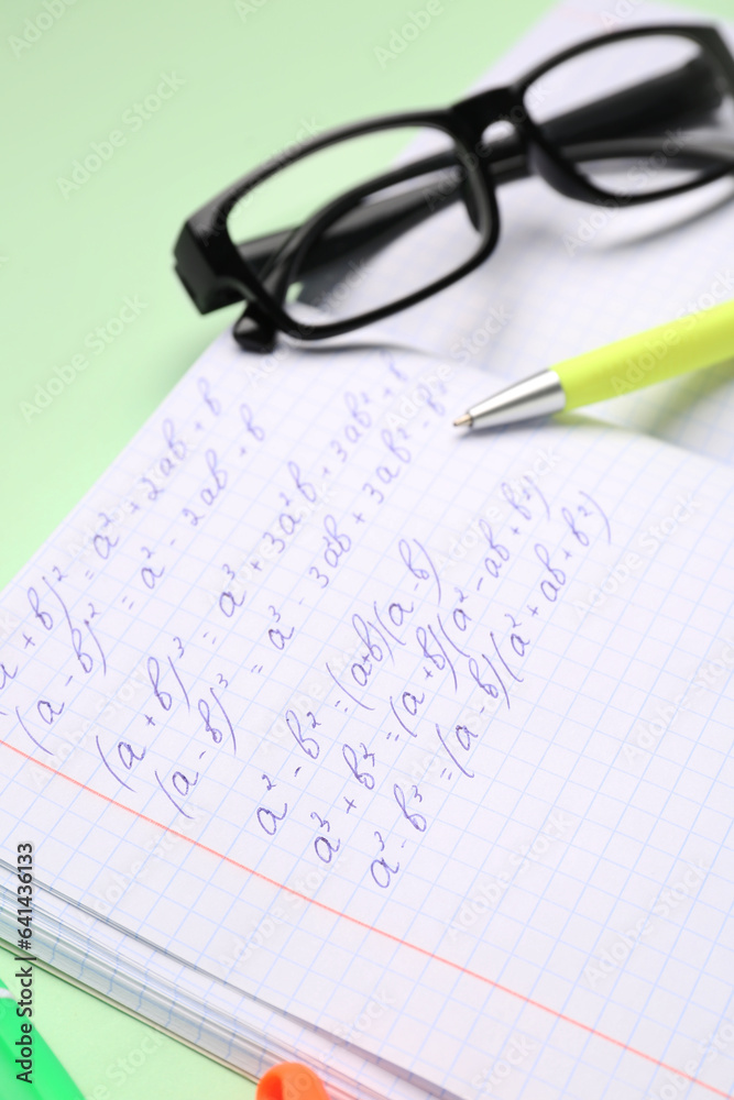 Copybook with maths formulas, glasses and pen on green background