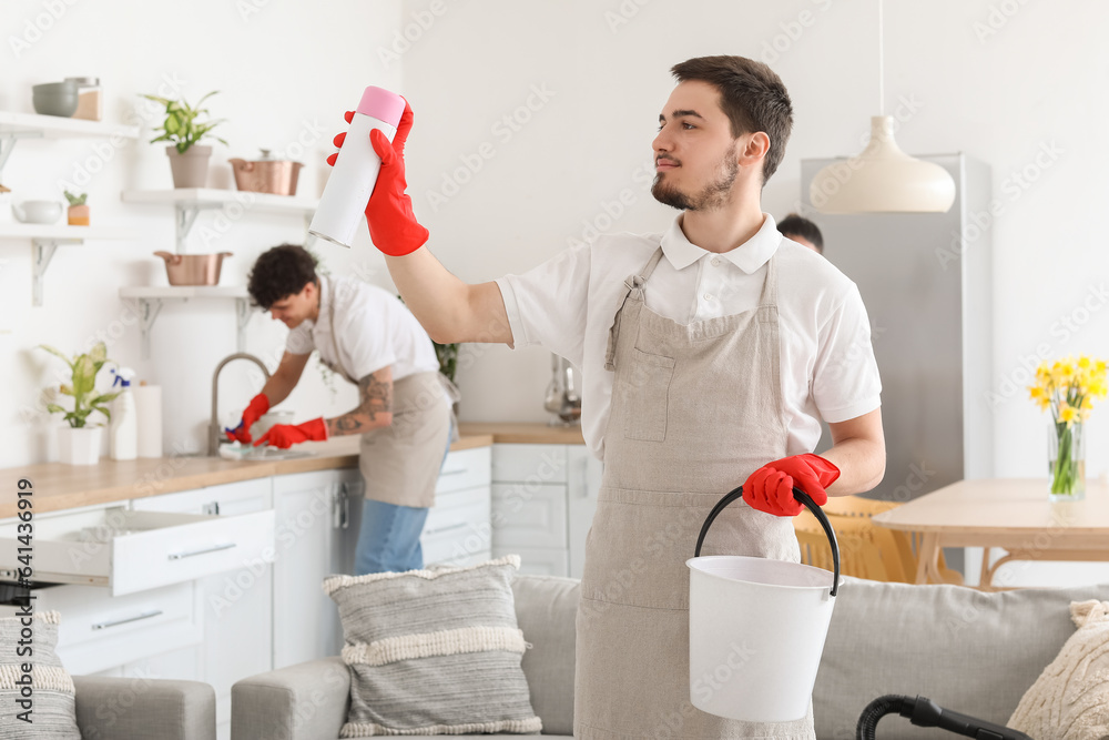 Male janitor with air freshener in kitchen