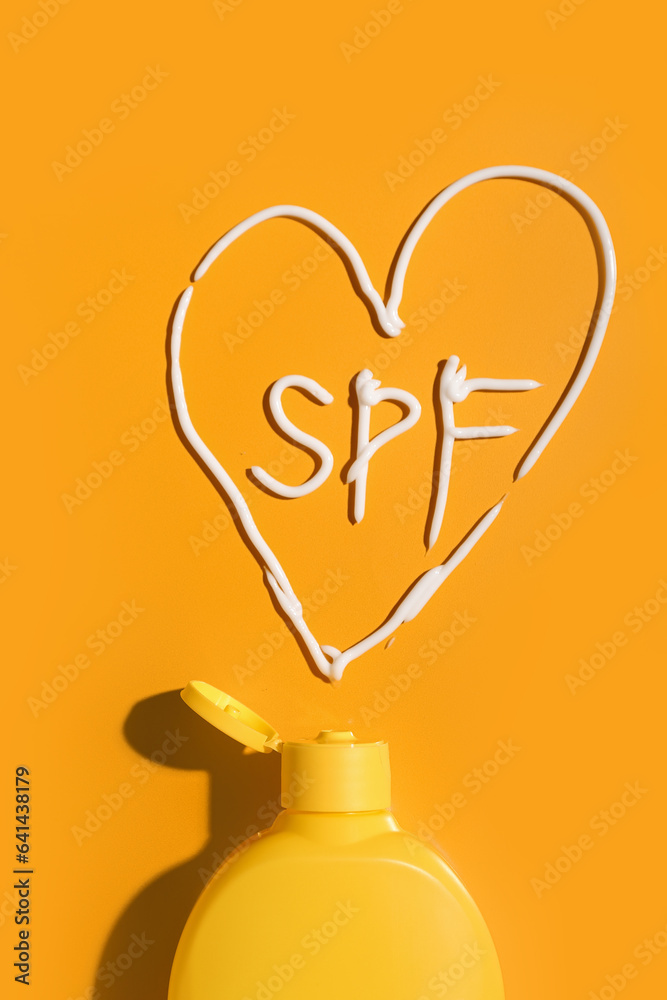 Drawing of heart and word SPF made with sunscreen cream on orange background