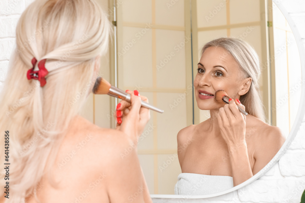 Mature woman doing makeup near mirror in bathroom