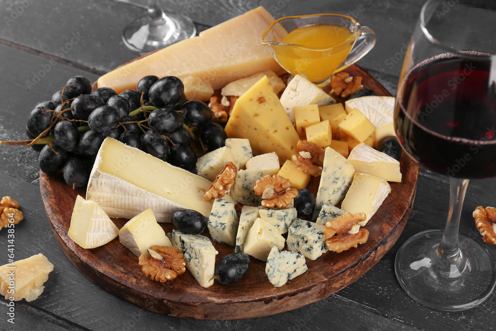 Plate with pieces of tasty cheese, grapes and honey on dark wooden background