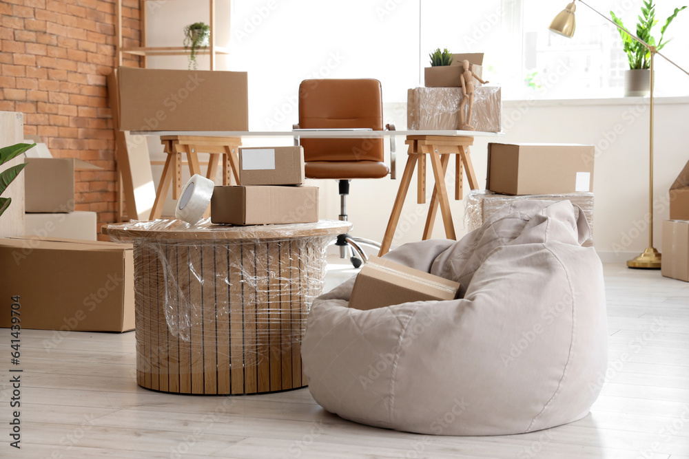 Coffee table and pouf with cardboard boxes in office on moving day