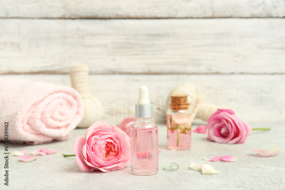 Bottles of cosmetic oil with rose extract and flowers on white table