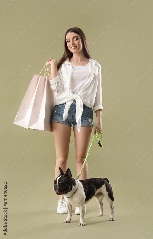 Young woman with shopping bags and her French bulldog on green background