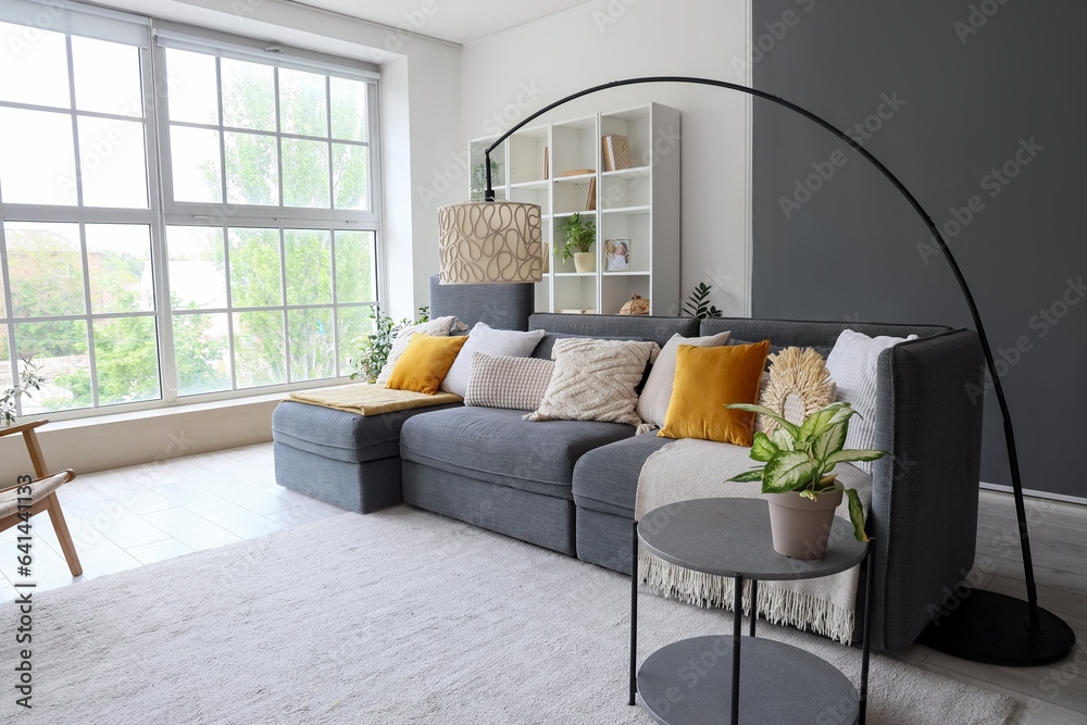 Interior of stylish living room with cozy grey sofa near big window