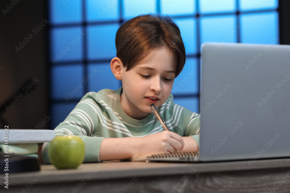 Little boy doing homework with laptop at home late in evening