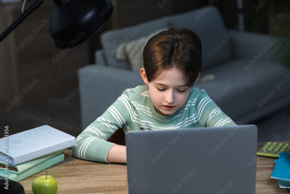 Little boy doing homework with laptop at home late in evening