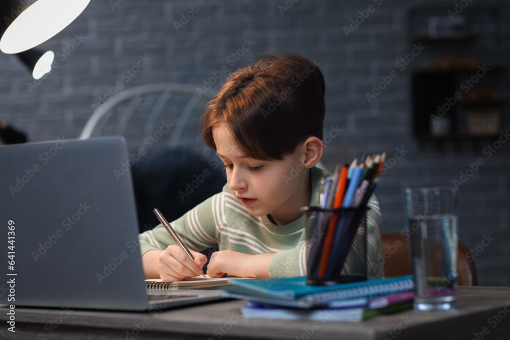 Little boy doing homework with laptop at home late in evening