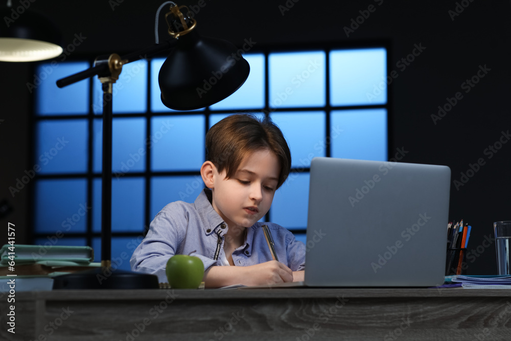 Little boy doing homework with laptop at home late in evening