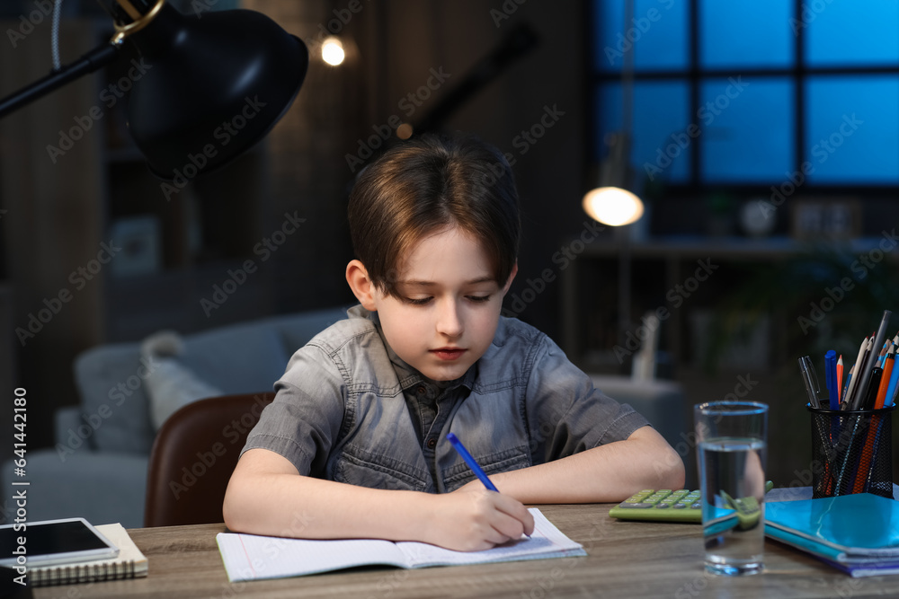 Little boy doing his homework at home late in evening